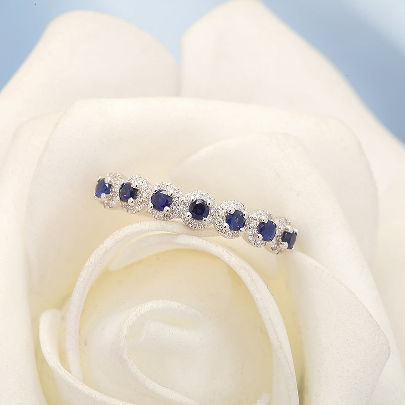 A silver wedding ring with 7 small lab grown sapphire encircled with moissanite halos.