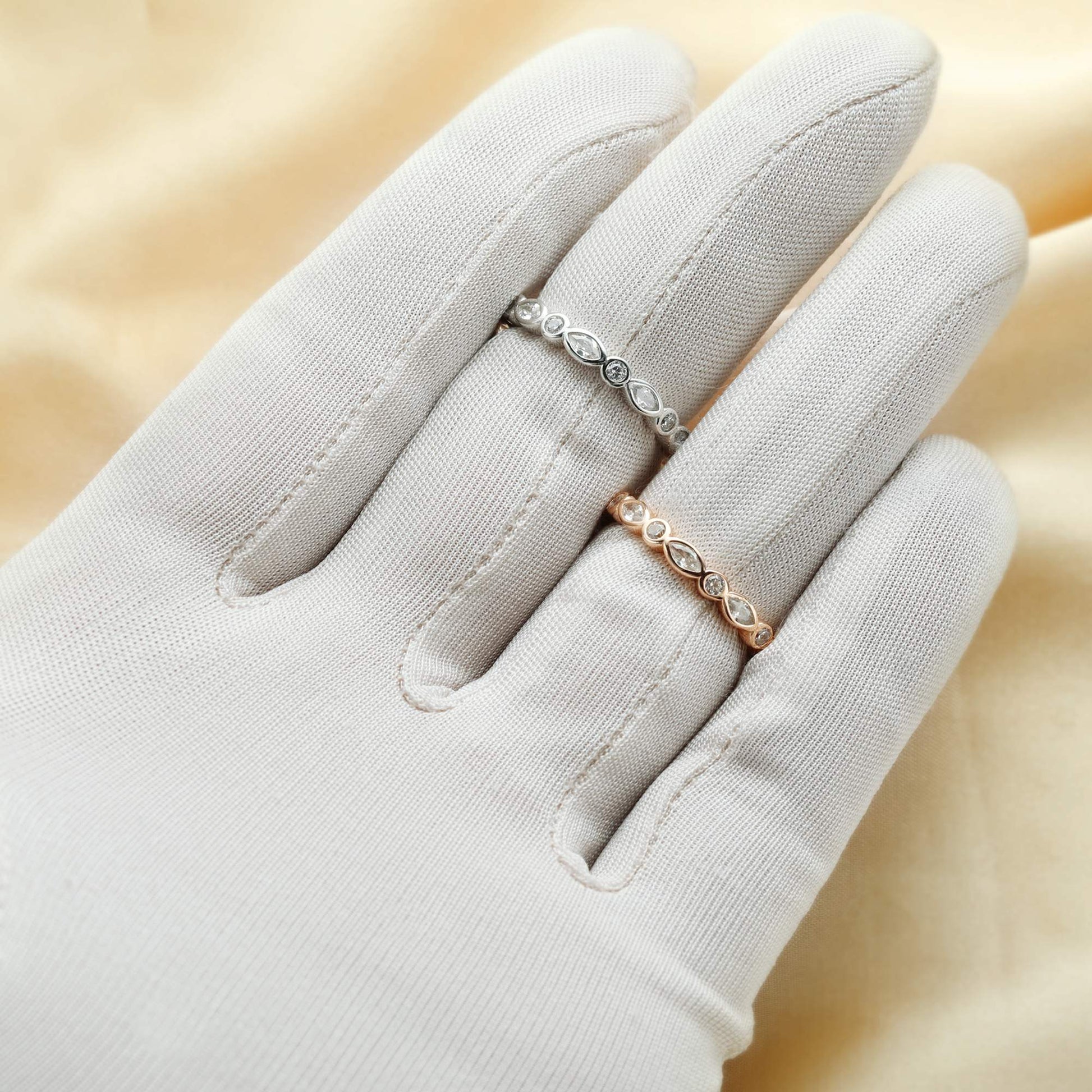 A hand wearing one silver and one rose gold ring bezel set with alternating marquise and round cut clear gems.