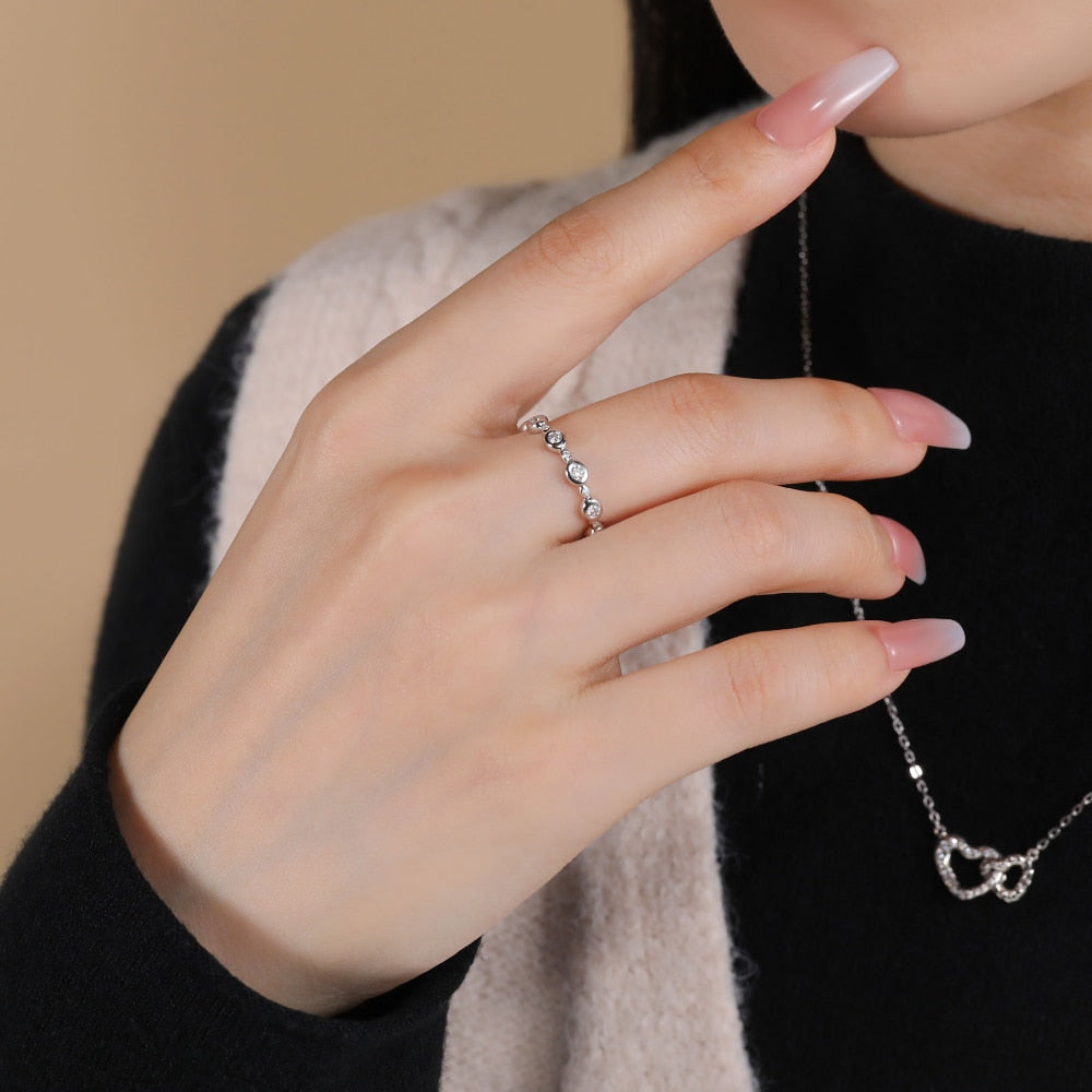 A hand wearing a silver bezel set eternity ring.