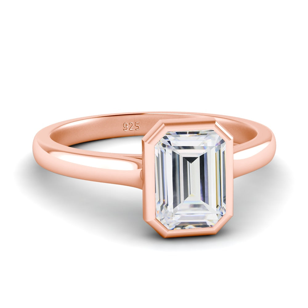 A rose gold bezel set emerald cut moissanite ring.