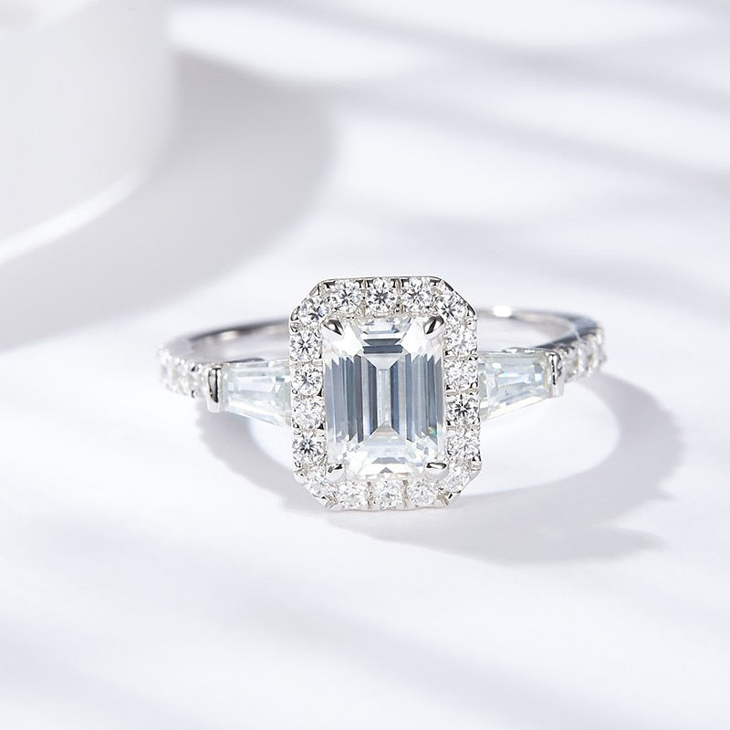 A silver engagement ring set with an emerald cut moissanite and is a hybrid 3 stone halo style.