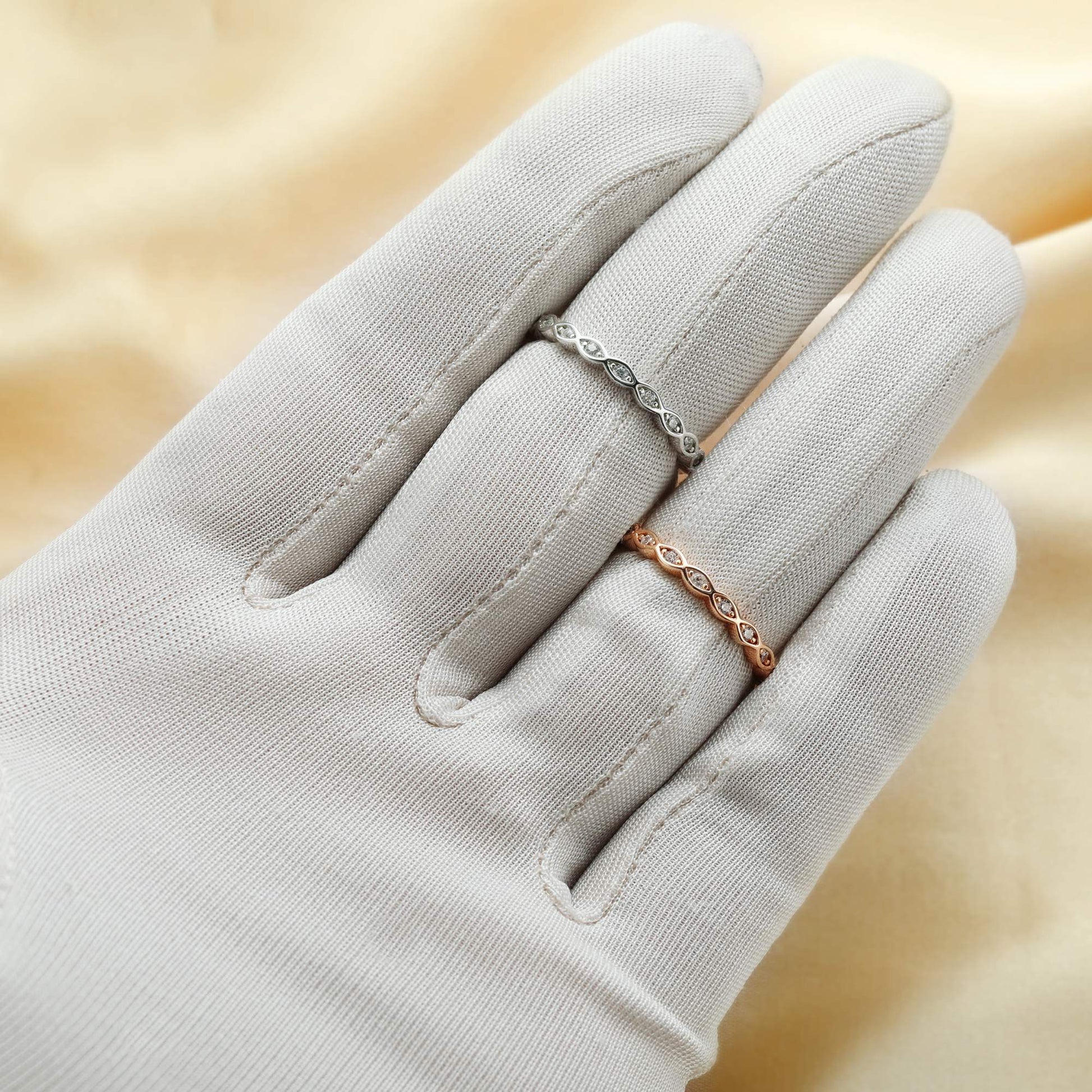 A hand wearing one silver and one rose gold scalloped ring band set with small clear stones.