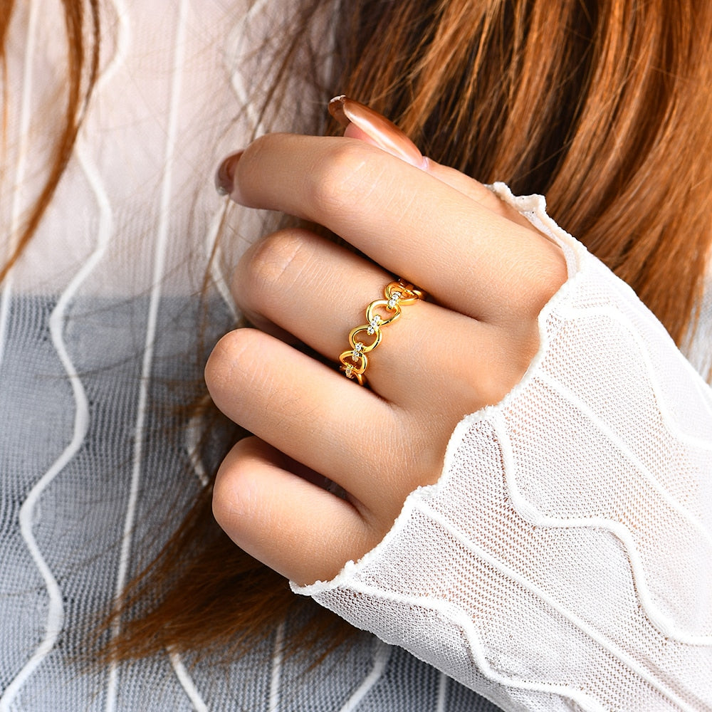 A hand wearing a gold chain link ring with 3 small moissanites connecting each link.