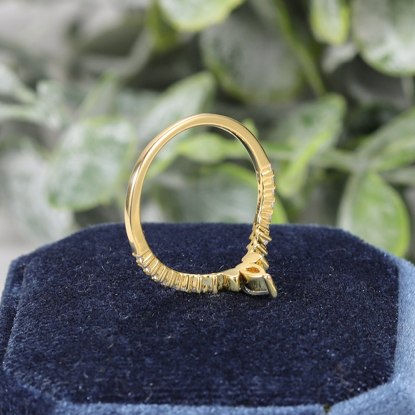 A gold chevron style wedding ring set with several small round moissanites set horizontally and two bezel set moissanites and one larger prong set moissanite at the V.