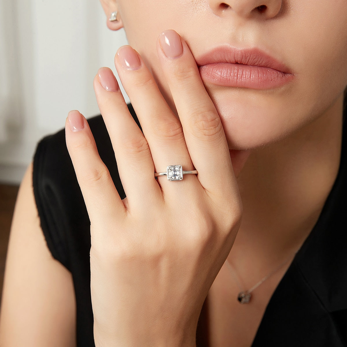 A hand wearing a silver Asscher cut bezel set engagement ring.