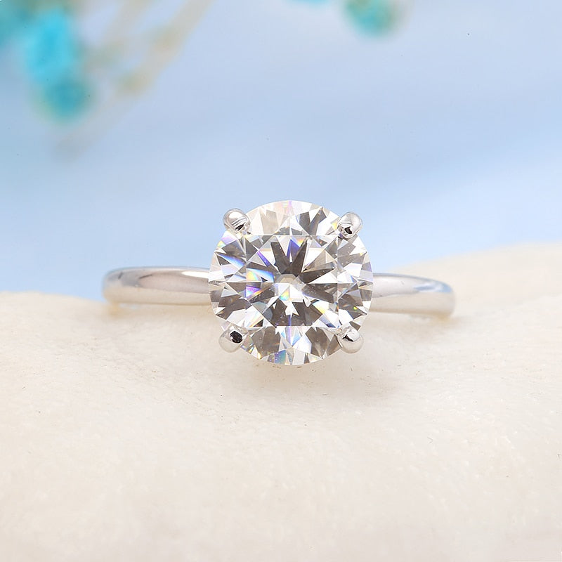 A silver slightly tapered band with a 4 prong setting; set with a 3CT round moissanite.