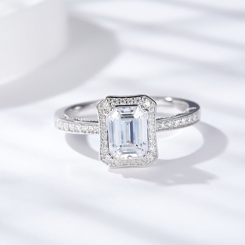 A silver halo ring set with an emerald cut moissanite.
