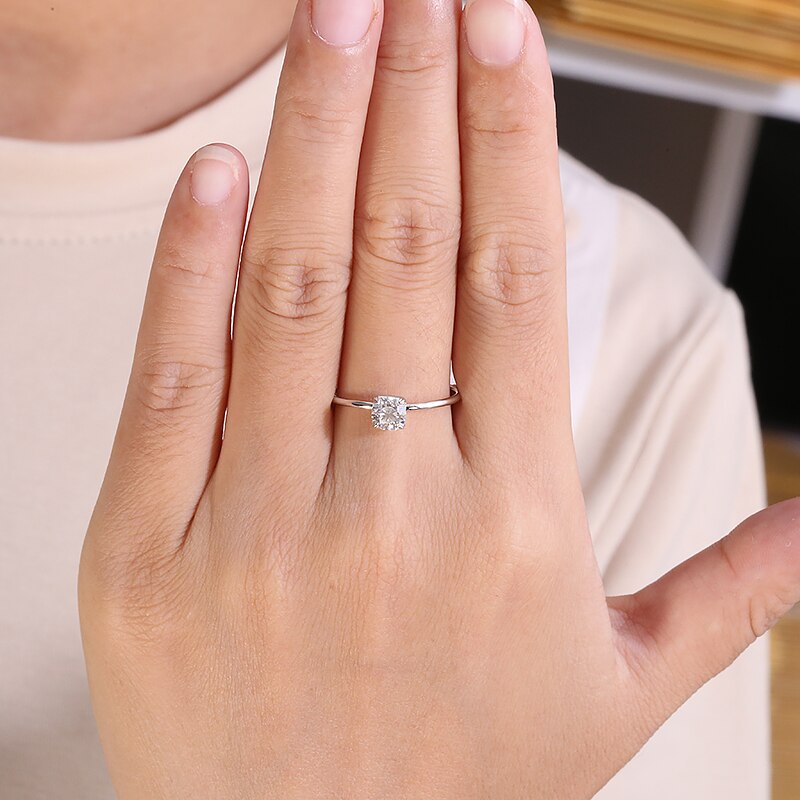 A hand wearing a silver solitaire with a squared basket.