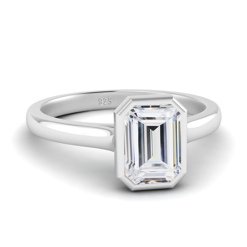 A silver bezel set emerald cut moissanite ring.