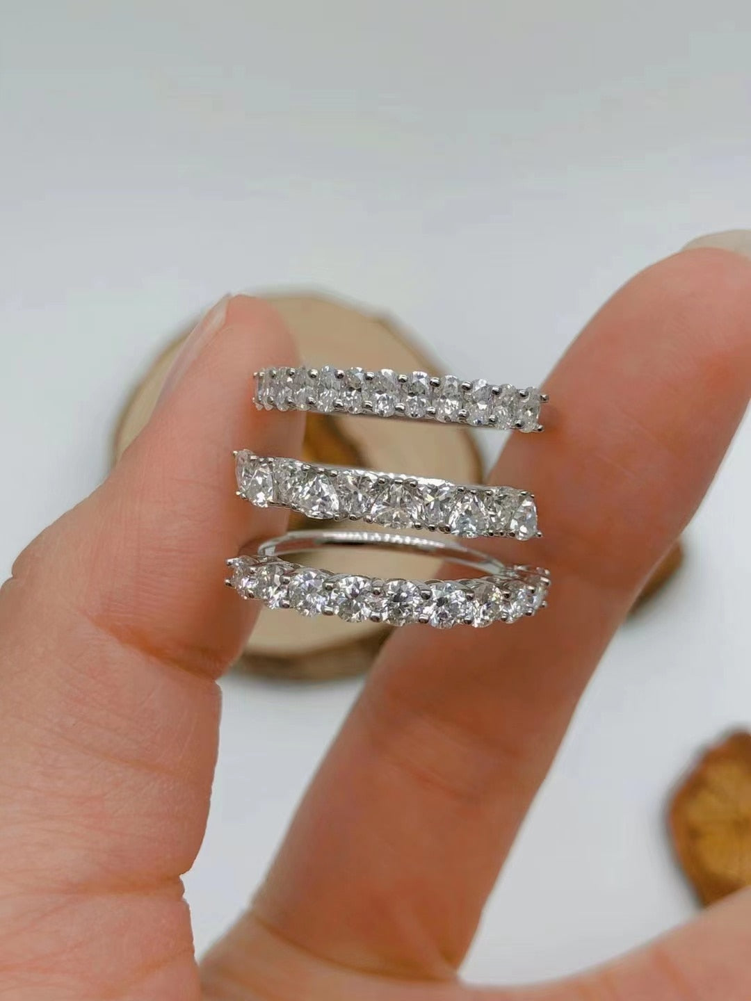 A hand holding half eternity rings with various cuts of moissanite.