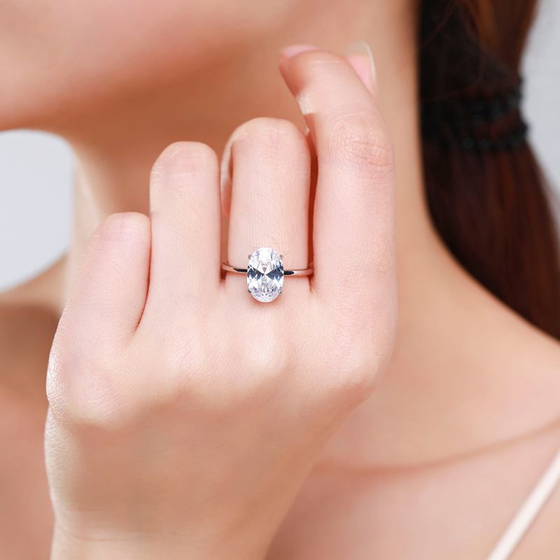 A hand wearing a silver solitaire ring set with a large oval moissanite.