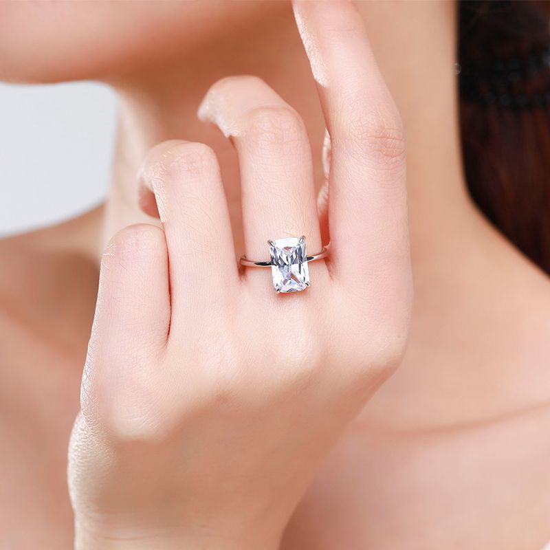 A hand wearing a silver large radiant cut solitaire engagement ring.