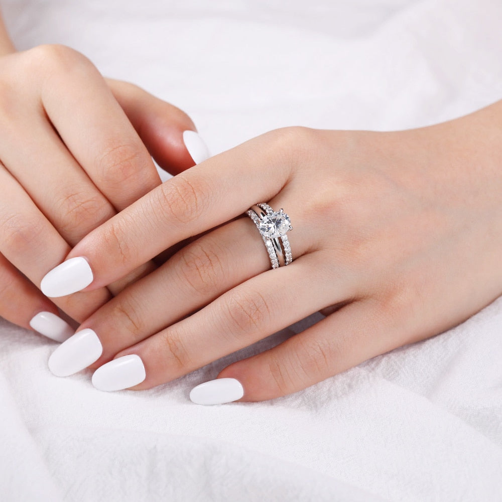 A hand wearing  a silver oval cut hidden halo engagement rings.