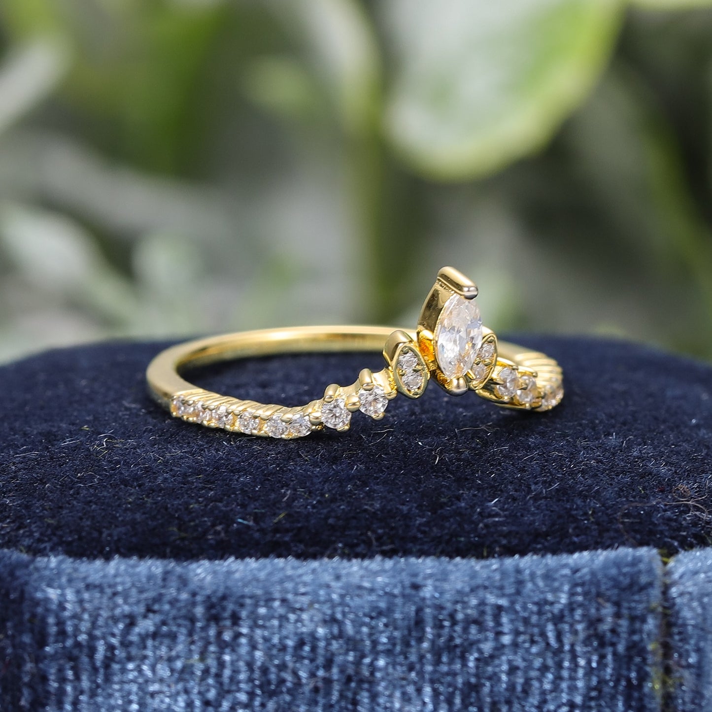 A gold chevron style wedding ring set with several small round moissanites set horizontally and two bezel set moissanites and one larger prong set moissanite at the V.
