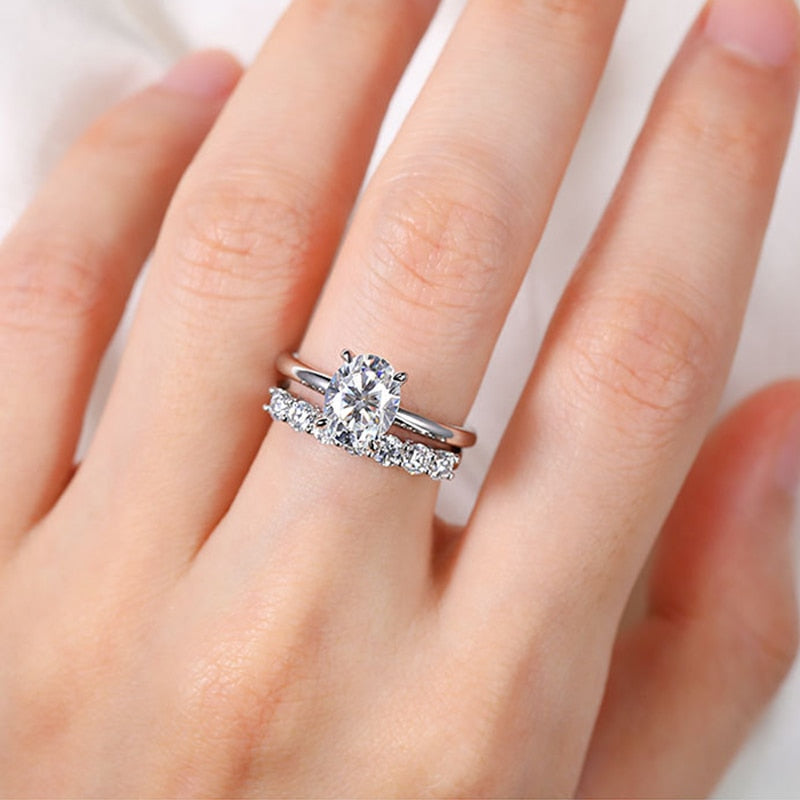 A hand wearing a silver oval cut hidden halo engagement rings.