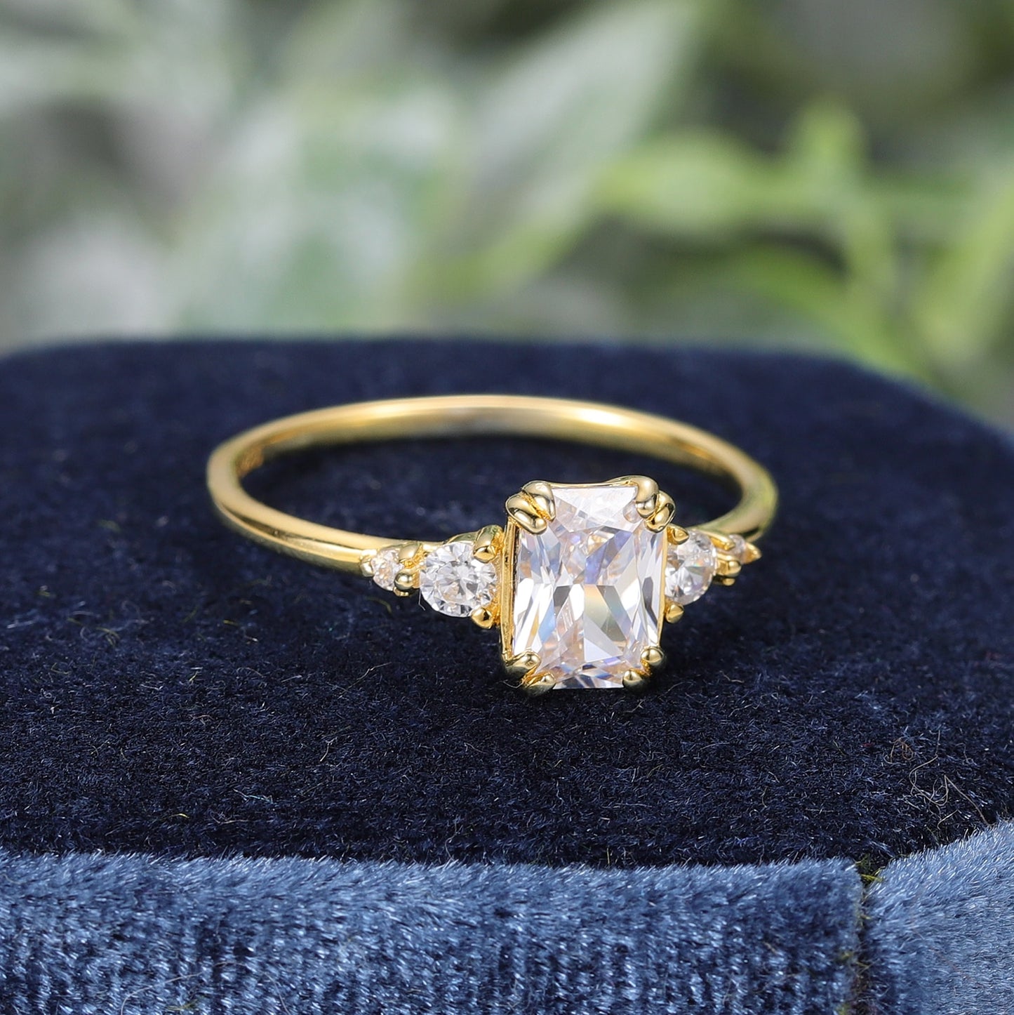 A gold ring set with a radiant cut moissanite with zircons on both sides.