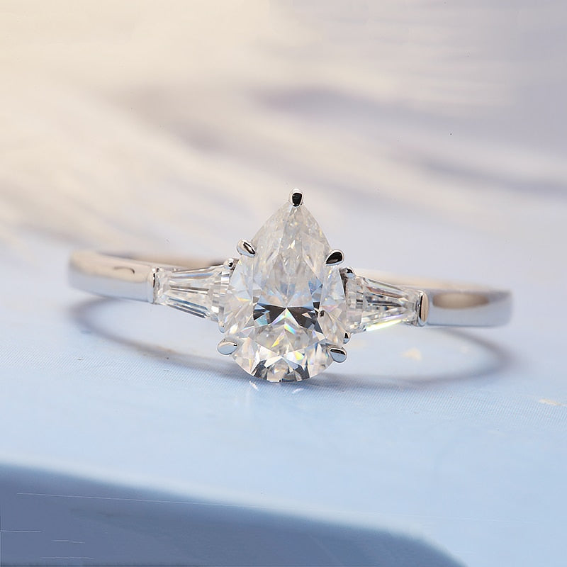 A silver 3 stone ring set with a 1.5CT pear cut moissanite set between two smaller baguettes.