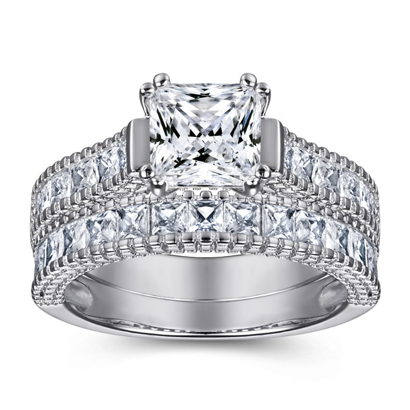 A silver engagement ring set with a princess cut moissanite on a princess cut pave style shank with a matching wedding band.
