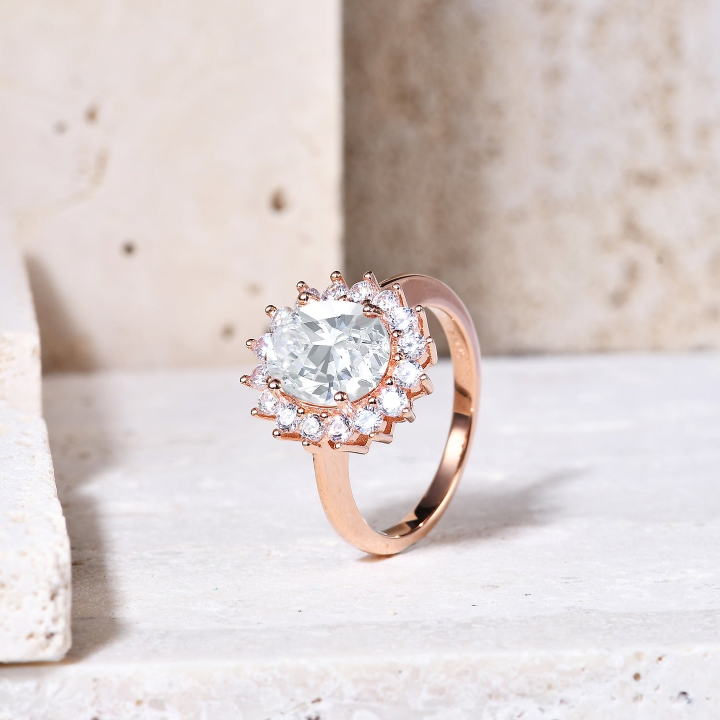A rose gold halo ring set with a 3CT oval cut moissanite set in the middle of a ring of clear gems.