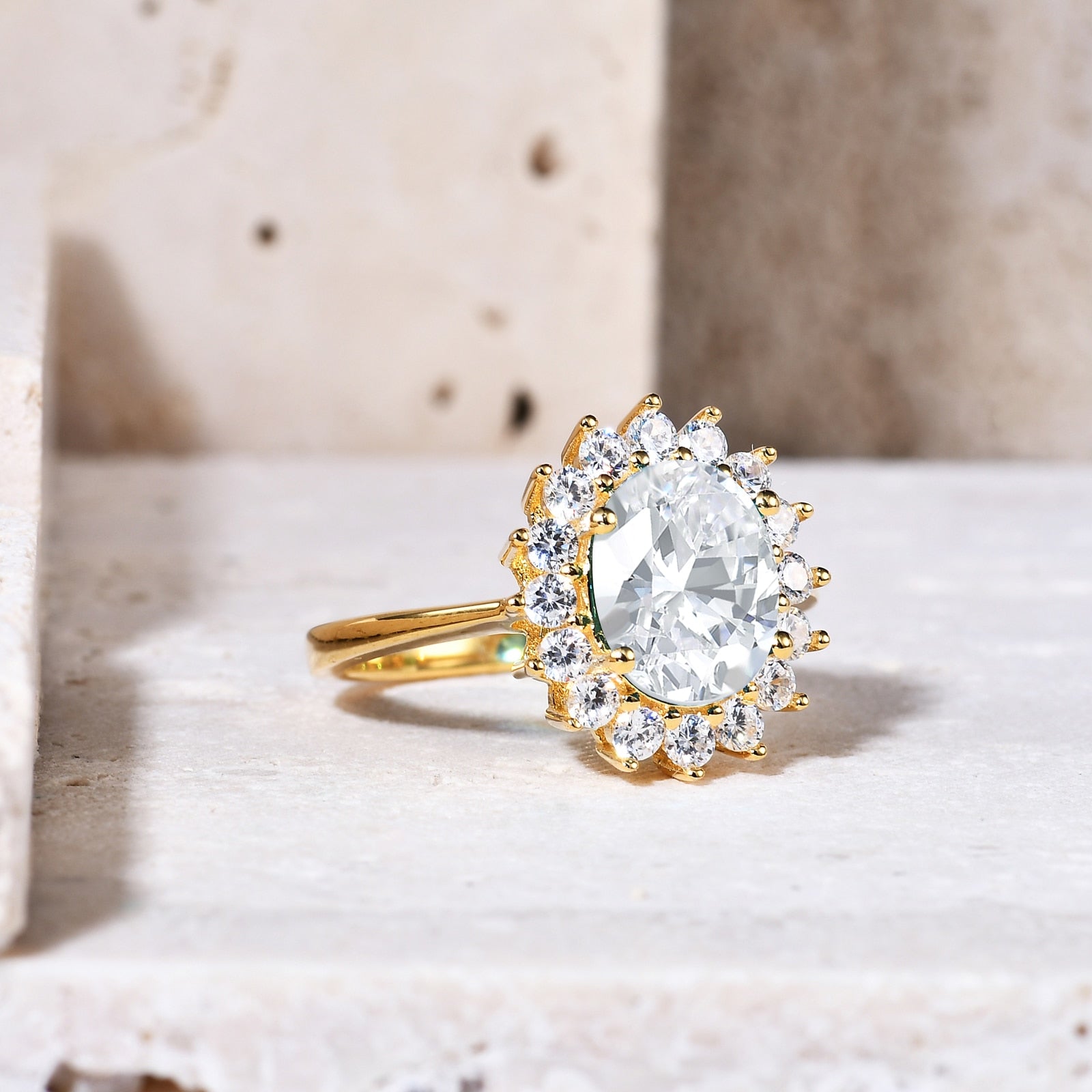A gold halo ring set with a 3CT oval cut moissanite set in the middle of a ring of clear gems.