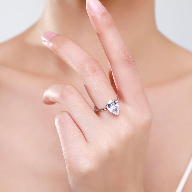 A hand wearing a silver solitaire ring set with a large pear cut moissanite. 