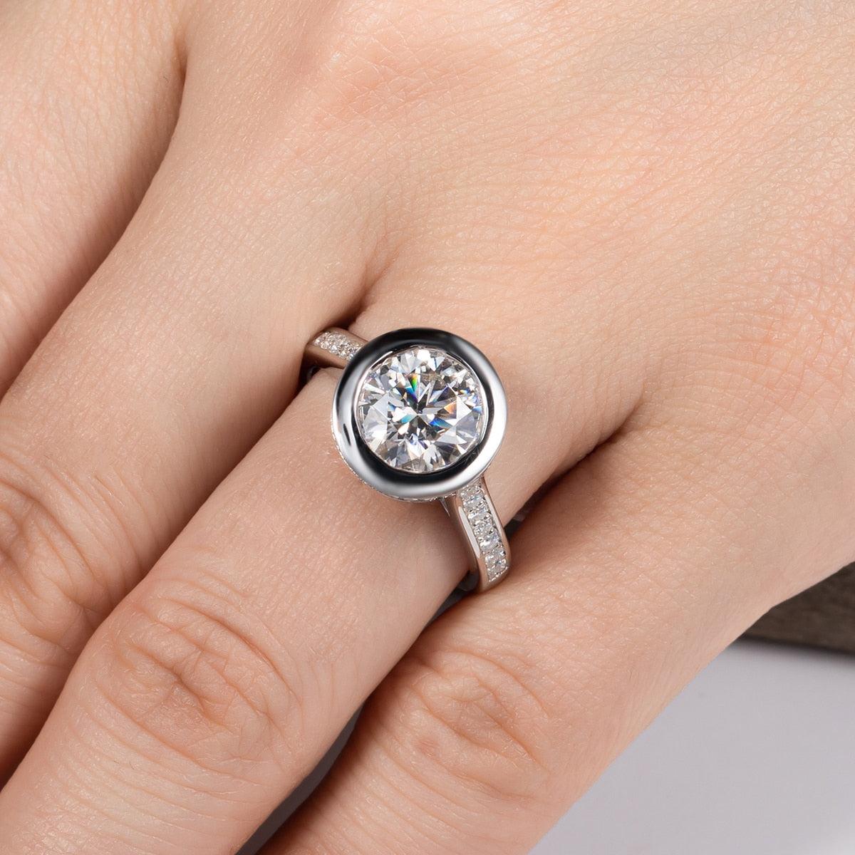 Hand wearing a 3CT moissanite, bezel set in a floating setting on a pave band.