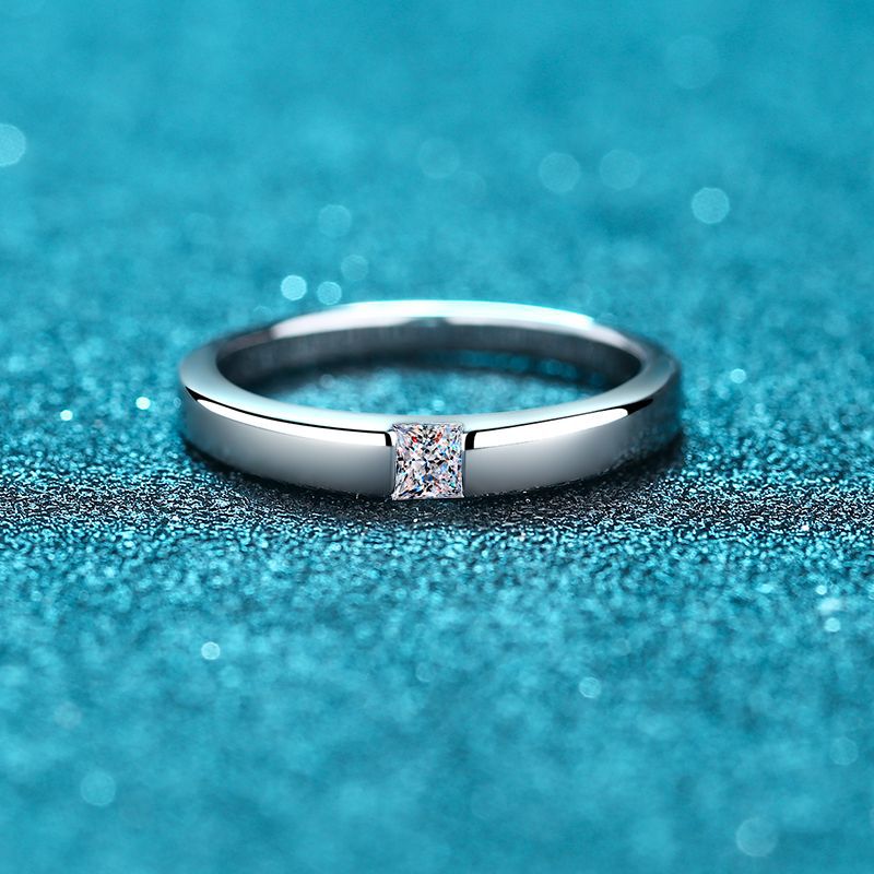 A silver ring tension set with a small princess cut moissanite.