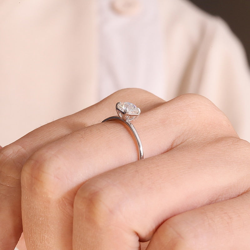 A hand wearing a silver solitaire with a squared basket.