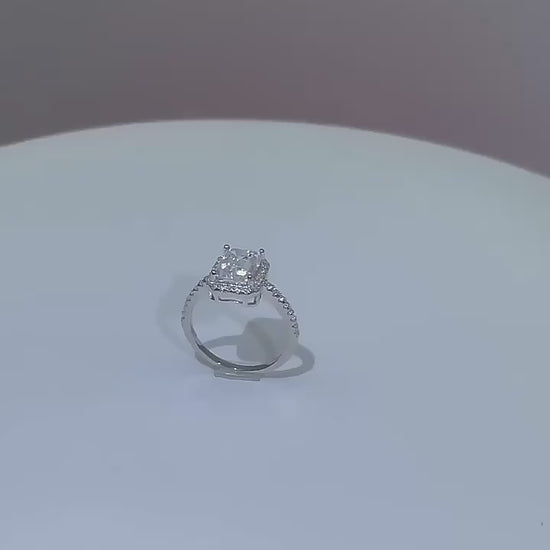 A silver halo ring set with a radiant cut moissanite spinning on a viewing platform.
