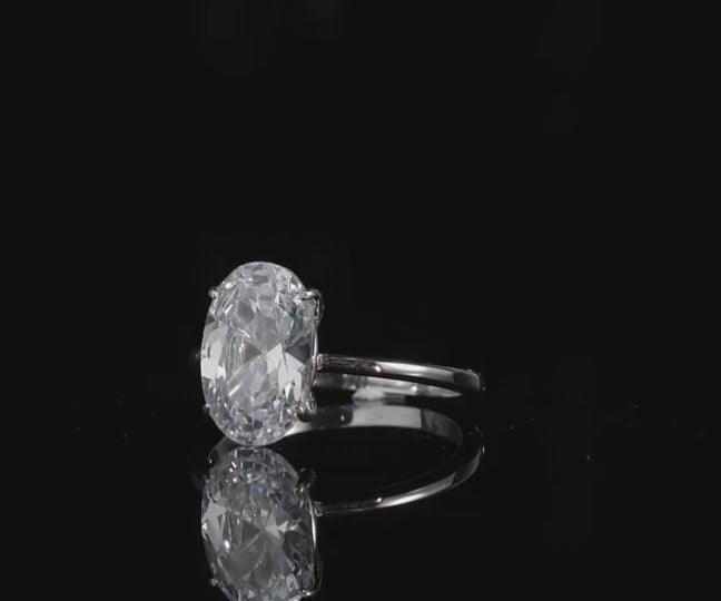 A silver oval cut moissanite ring spinning on a viewing platform.
