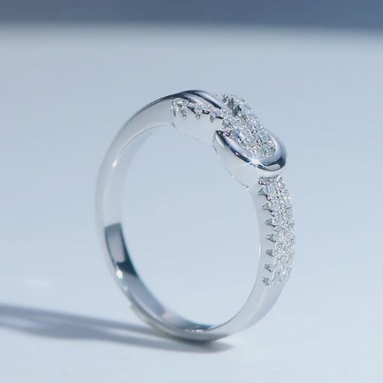 A silver half pave infinity knot ring spinning on a viewing platform.