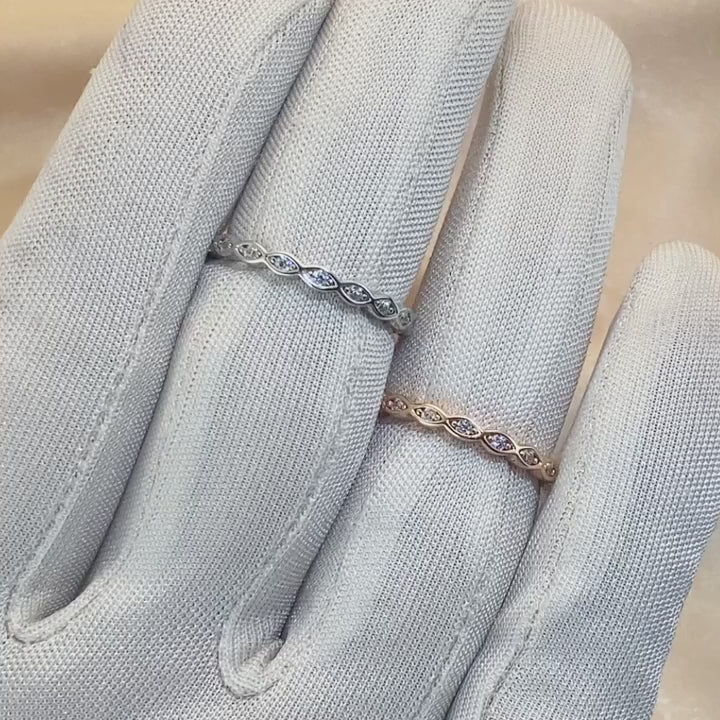 A hand wearing and displaying one silver and one rose gold scalloped ring band set with small clear stones.