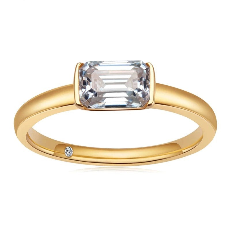 A gold tone ring set with a emerald cut moissanite set east to west in a tension bar setting.